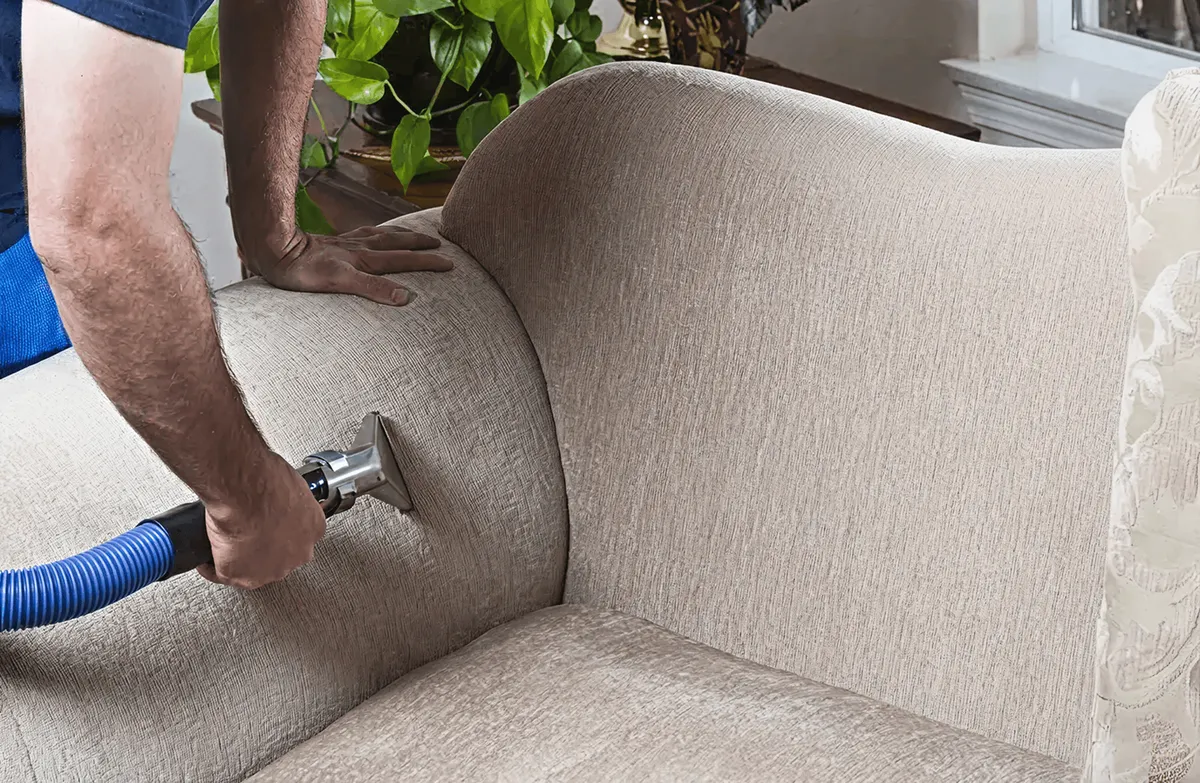 Professional upholstery cleaner deep-cleaning a fabric sofa with a handheld extraction tool and hose, Fort Wayne, IN.